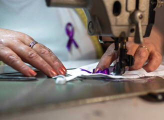 Working woman, woman sewing purple ribbon on face masks. women's Day. Gender violence