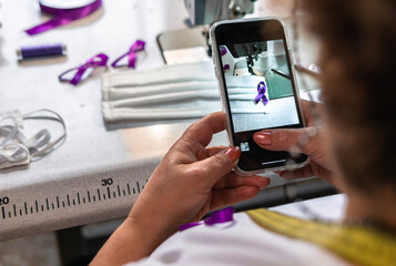 Working woman, woman taking photo of a purple ribbon sewn on masks. women's Day. Gender violence