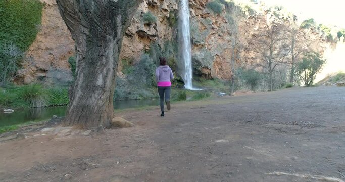 Mujer adulta haciendo deporte junto a r&iacute;o y bella y alta cascada de agua