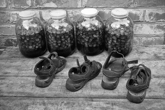 A country courtyard, against the wall of a red brick house, there are four three-liter jars of strawberry compote. Childrens shoes are standing in front of the banks.