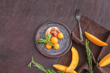 Plate with delicious melon and prosciutto on dark background