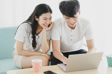 Young couple sitting watching laptop together with happy expression