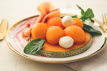 Plate with delicious melon, mozzarella and prosciutto on light background