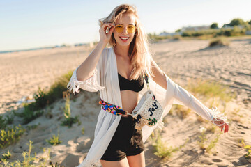 Summer mood. Graceful carefree blonde girl on trendy boho beach cover with fringe and accessories ...