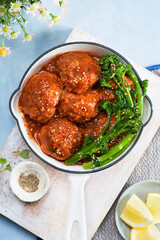 Tikka Masala Meatballs with broccolini, broccoli florets green vegetable baby broccoli, in cast iron pan, vegan healthy dinner, lunch on light blue background. Close-up. Top view, indian food recipe.