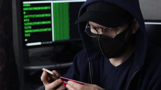 male hacker in a mask and a cap is engaged in cybercrime, stealing money from payment cards.