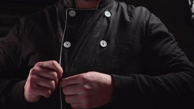 The Chef zips up his jacket. Close-up on a black background.