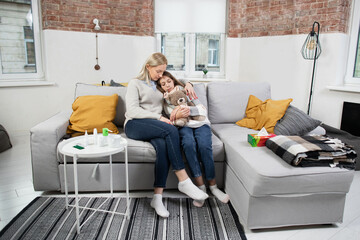 Flu, coronavirus and cold concept. Full length view of worried blond 40-aged mother, hugging her sick tired teen girl daughter and checking her temperature