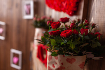 Red and pink potted roses stand on a wooden shelf against a background of brown wooden walls. A potted plant in a festive package. Gifts for Valentine's Day-a red rose in a pot.