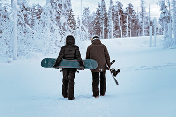 Two frends snowboarders are walking through the winter forest. Snowboarding in the forest in the...