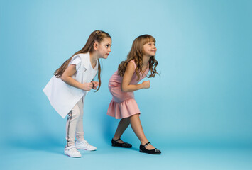 Happy kids, girls isolated on blue studio background. Look happy, cheerful. Copyspace for ad. Childhood, education, emotions, business, facial expression concept. Ready to run, start up