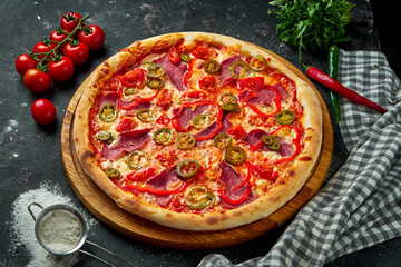 Appetizing italian pizza with ham, cheese, jalapenos, tomatoes and bell pepper in a composition with ingredients on a black background