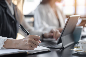 Close-up image of a businesswoman taking notes and using tablet on the desk at office.