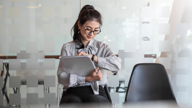 Young Asian businesswoman holding a portfolio looks at the clock waits for a job interview at the office.