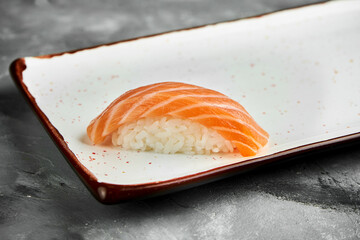 Classic Japanese sushi with raw salmon on a white plate on a gray background. Japanese cuisine. Close up, selective focus