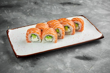 Japanese sushi roll - Philadelphia with salmon, cream cheese and avocado on a white plate on a gray background. Japanese cuisine. Close up