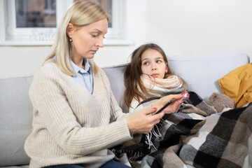 Sick child. Cute teen girl, lying on the sofa at home with scarf around neck, covered with blanket...