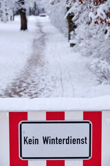 A red and white sign on a footpath at the entrance of a park informs about Kein Winterdienst  (in English: no winter maintenance). Seen in  Bavaria in Germany in February.