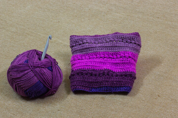 colorful ball of wool and piece of woven winter garment with crochet needle or hook against light background. copy space background for crochet knitting hobby.