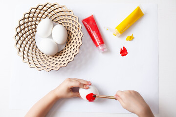 painting eggs happy easter child's hands paint an egg with a brush on a white background general plan preparing for easter. 
the inscription on the tube of paint: red