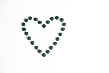green pills lined with heart shaped spirulina dietary supplements healthy lifestyle vitamins benefit white background