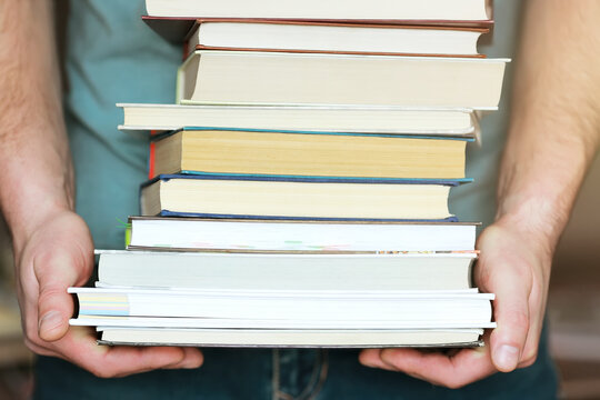 A man holds a stack of books in his hands. A photo without a face. A lover of reading. Close-up