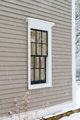 Fototapeta premium A vintage double hung window with reflecting glass on a beige colour exterior wall of a building. The window has a dark green with white trim. There's a rock foundation below the wood clapboard wall.