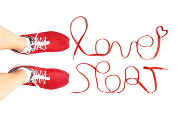 Cropped view of female feet wearing red running sneakers and lettering "love sport" made of athletic shoelaces isolated on white background. Active lifestyle concept.