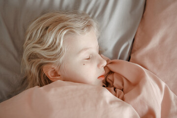 Closeup of cute Caucasian blonde girl child sleeping dreaming in bed at home. Sleep tired kid with closed eyes under pink blanket in a bedroom. Morning routine. Sweet dreams.