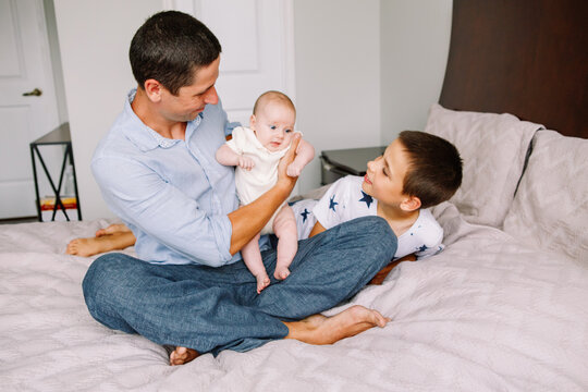 Fathers Day holiday. Caucasian father dad holding newborn baby. Brother playing with sister. Siblings relationship. Man parent spending time with children kids. Authentic lifestyle family moments.