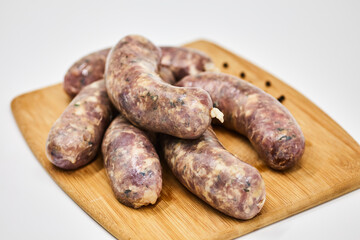 Raw sausage semi-finished products lie on a wooden board, isolated on a white background. The concept of cooking from semi-finished products. Italian traditions, Bavarian sausages, German sausages