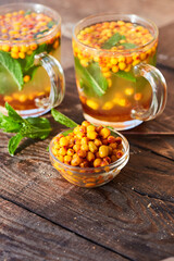 Warming green tea with sea buckthorn and mint, poured into glass mugs stands on a wooden table. The concept of a therapeutic healing drink prepared in glass