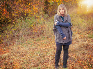 A woman of 40 years in autumn nature landscape. The blonde woman wears clothes made of wool and boots. - obrazy, fototapety, plakaty