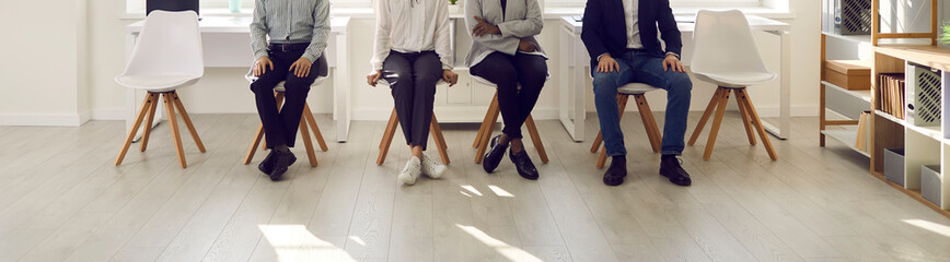 People are waiting in the waiting room. Cropped image of the legs of various people sitting on chairs and waiting their turn for an interview. Concept of employment, clients and human resources. - obrazy, fototapety, plakaty