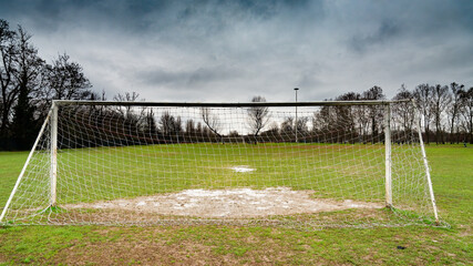 Fototapeta premium Goal post from behind in an abandoned soccer field. Dramatic stormy sky on the horizon.