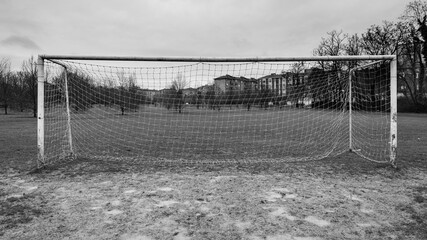 Goal post with net of an abandoned soccer field during a rainy day. Muddy ground. Monochromatic.