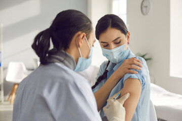 Fototapeta Young woman in medical face mask getting flu or COVID-19 vaccine injection. Doctor giving shot to female patient during vaccination campaign due to Coronavirus pandemic or seasonal infection outbreak obraz