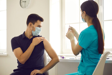 Immunization and vaccination concept. Doctor preparing flu or Covid-19 vaccine injection. Young man in medical face mask sitting at table at hospital waiting for nurse to get syringe ready for shot