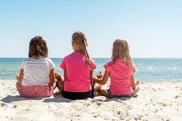 Back view three girls sitting on beach and looking at sea. Close-up Yoga asana, summer fun