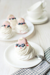 Pavlova meringue cake with fresh berries on white background. Tea cups and napkin on wood table