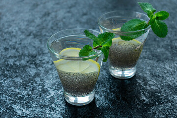 Chia seeds are washed down with water in a transparent glass with lemon and mint on a black background. Copy space.