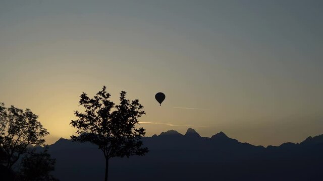 The balloon takes off over the line of mountains. A silhouette. The general plan. A small tree in the foreground.