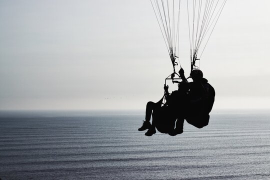 Silhouette Couple Paragliding Over Sea Against Sky