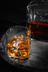 Barrel of scotch whiskey with a decanter of whiskey and glass of whiskey with ice on a black background. Bottle and glass of whiskey with ice on a wooden background