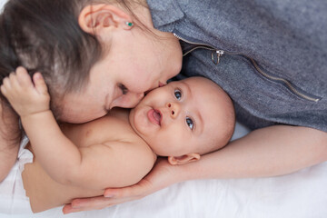 Portrait of a beautiful mom playing with her 5 month old newborn daughter in the bedroom, top view