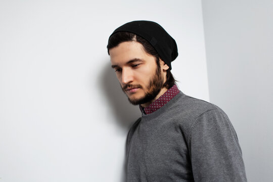Studio side portrait of young guy on white background. Man wearing grey sweater and black hat.