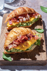 croissant sandwich breakfast with scrambled egg, crispy bacon and mashed avocado