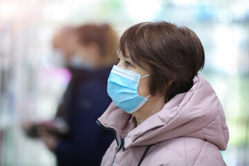 Portrait of an adult woman looking to the side wearing a medical mask on a blurred background in a store