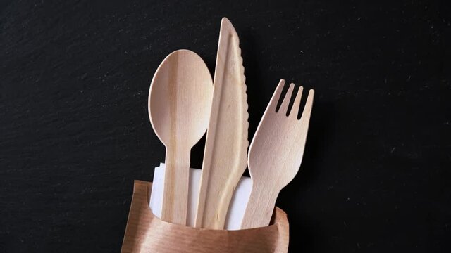 Disposable biodegradable tableware made of wood spoon, knife and fork on marble texture. Close-up.