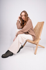 Young attractive woman with long hair in pastel casual clothes sitting on chair. Caucasian girl posing on white background, side view